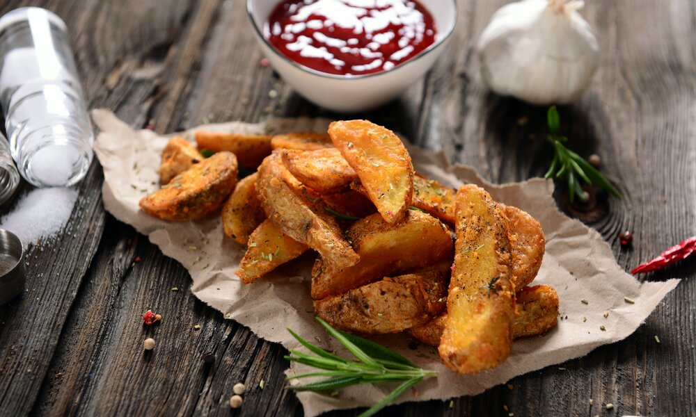 Knusprige Kartoffelwedges auf gerissenen Backpapier, daneben Salz und weitere Gewürze. | © Adobe Stock / Piotr Krzeslak