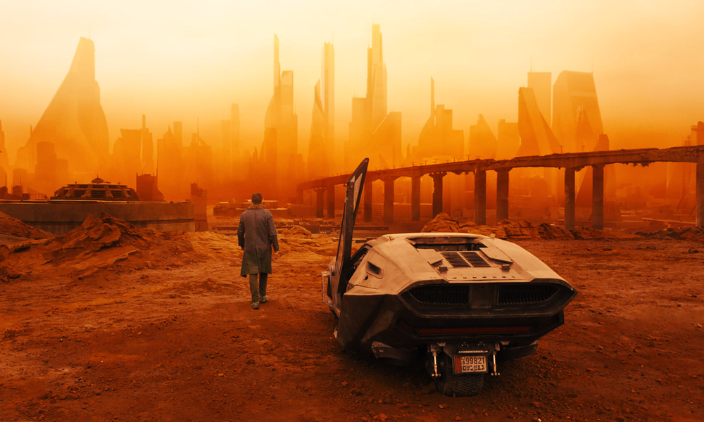 Blick auf ein Raumshuttle und einen Mann, der auf eine futuristische Stadtsilhouette im Hintergrund zugeht - alles ist in rötliches Licht getaucht. | © ddp images/Warner Bros./Everett Collection