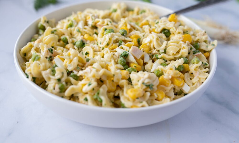 Nudelsalat in der Nahaufnahme in einer weißen Schüssel, mit Mayonnaise und Erbsen. | © Adobe Stock / Angelika Heine