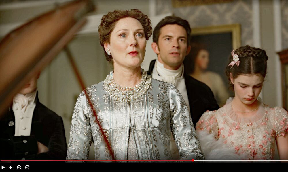 Ruth Gemmel als Lady Bridgerton, Jonathan Bailey als ihr Sohn Anthony und Florence Hunt als ihre Tochter Hyacinth stehen in einer Szene der dritten Staffel der Netflix-Serie "Bridgerton" hinter einem Klavier. | © Netflix/Screenhot Video