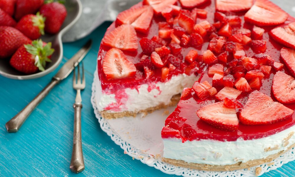 Erdbeer-Schmand-Kuchen in Nahaufnahme, aufgeschnitten und mit frischen Erdbeeren bestückt. | © Getty Images / 	tanialerro