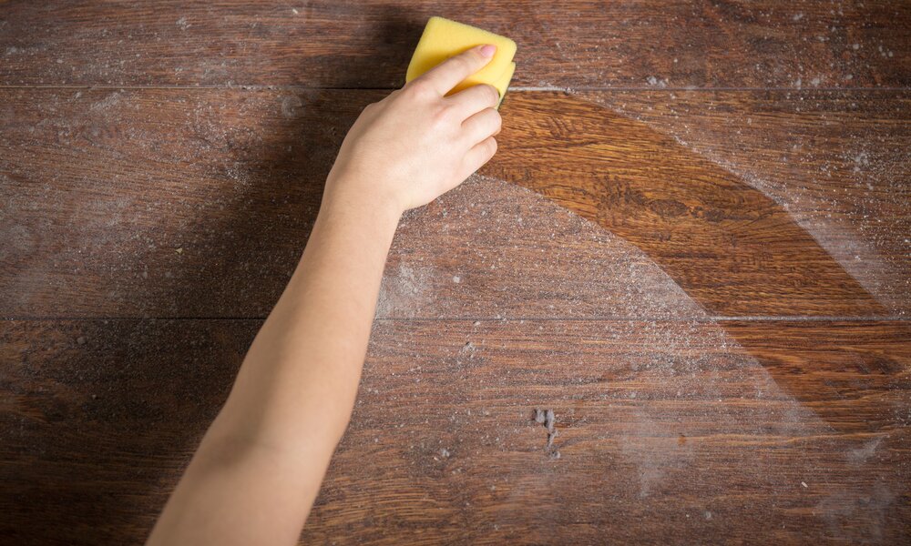 Eine Hand reinigt mit einem Schwamm einen staubigen Holztisch, der klare Kontrast zeigt den Unterschied. | © Adobe Stock/ Photographee.eu