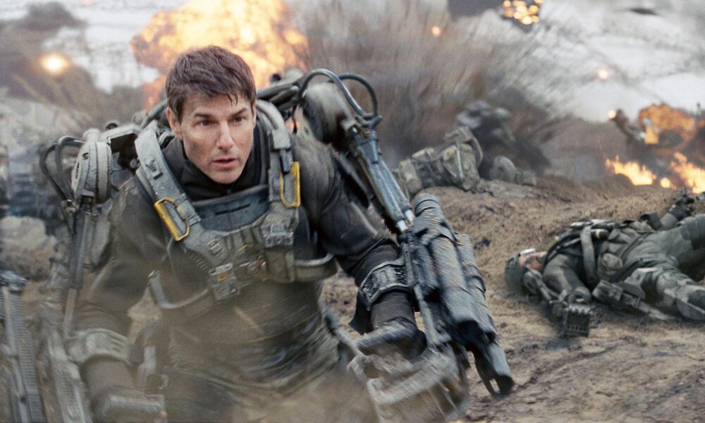 Rom Cruise läuft in militärischer Ausrüstung auf die Kamera zu in einer Szene aus dem Kinofilm "The Edge of Tomorrow" - im Hintergrund Explosionen. | © Imago Images/Cinema Publishers Collection