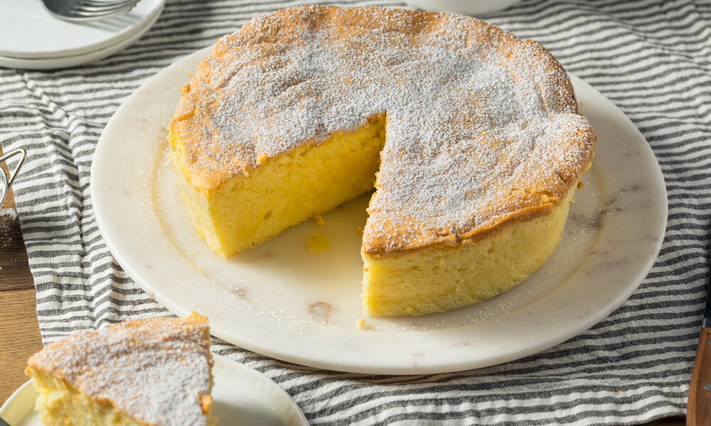 Angeschnittener Quarkkuchen auf einem weißen Kuchenteller auf einem Holztisch. | © Getty Images / 	bhofack2
