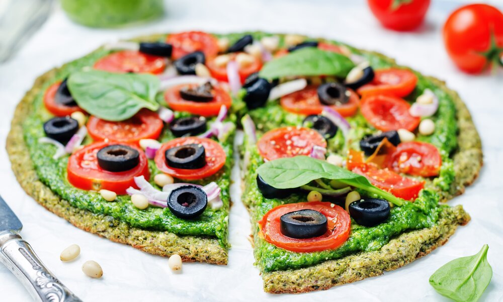 Angeschnittene Low Carb Zucchini-Pizza ohne Mehl, belegt mit Oliven, Tomaten, Basilikum und Pinienkerne. | © Adobe Stock / nata_vkusidey