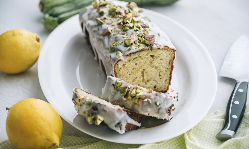 Angeschnittener Joghurtkuchen mit Zitronenguss und Pistazien on top, daneben frische Zitronen. | © Getty Images / Westend61