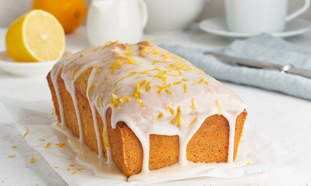 Rechteckiger Zitronen-Joghurtkuchen mit Glasur und garnierten Zitronenzesten. | © Adobe Stock / Nata Bene