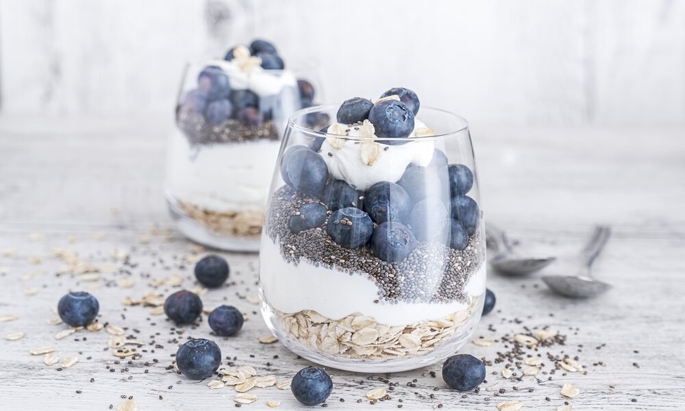 Zwei in Gläsern angerichtetes Müsli bestehend aus Haferflocken, Blaubeeren, Chiasamen und Quark. | © Getty Images / Tina Terras & Michael Walter