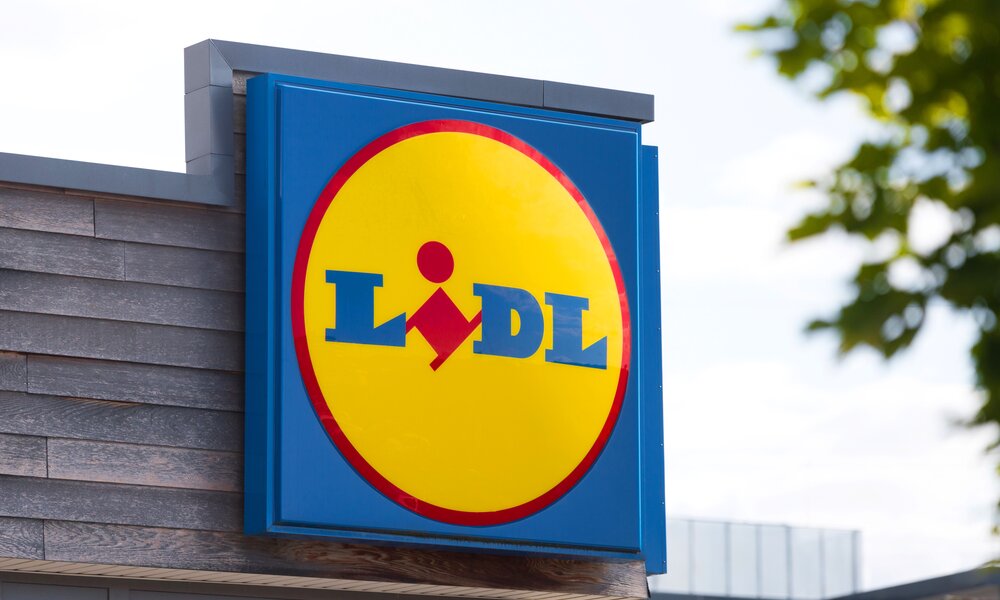 Logo der Supermarktkette Lidl in blau und gelb an einer Holzfassade bei Sonnenschein. | © Adobe Stock / Tobias Arhelger