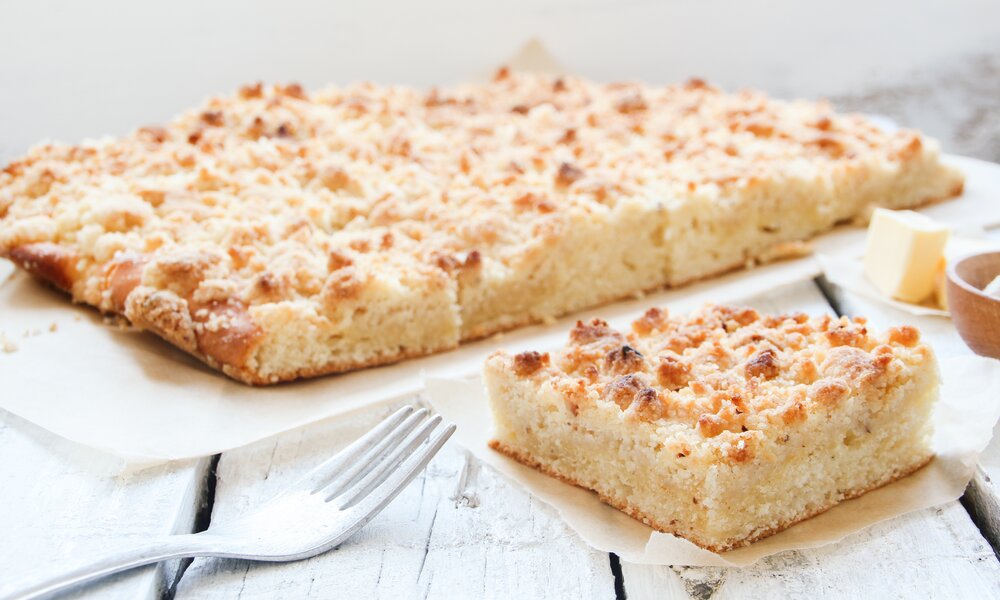 Angeschnittener Streuselkuchen auf Holzuntergrund, daneben ein Stück Kuchen und eine Gabel. | © Adobe Stock / eflstudioart