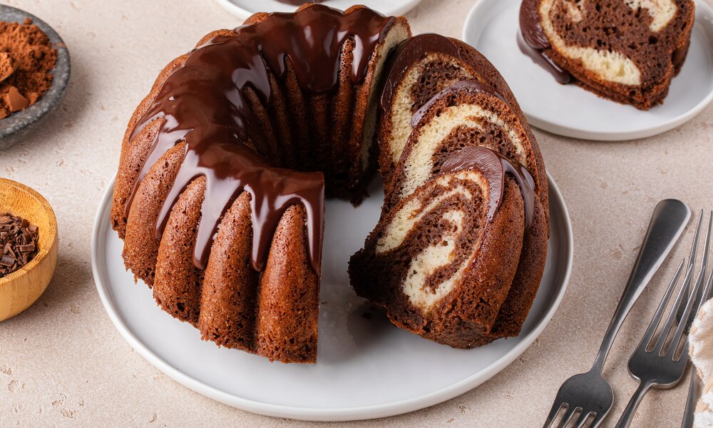 Angeschnittener Marmorkuchen  mit Schokoladenglasur auf einem weißen Teller angerichtet. | © Getty Images / 	VeselovaElena
