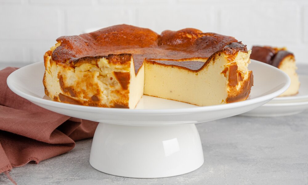 Angeschnittener Käsekuchen auf einem Tortenboden auf einer Tisch angerichtet. | © Getty Images / Irina Taskova