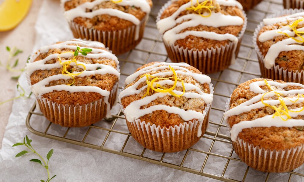 Mehrere Zitronenmuffins auf einem Abkühlgitter mit Guss verziert, daneben frische Kräuter. | © Getty Images / VeselovaElena