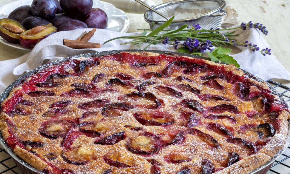 Pflaumenkuchen in Kuchenform, daneben frische Pflaumen und etwas frischer Lavendel. | © Getty Images / 	alle12