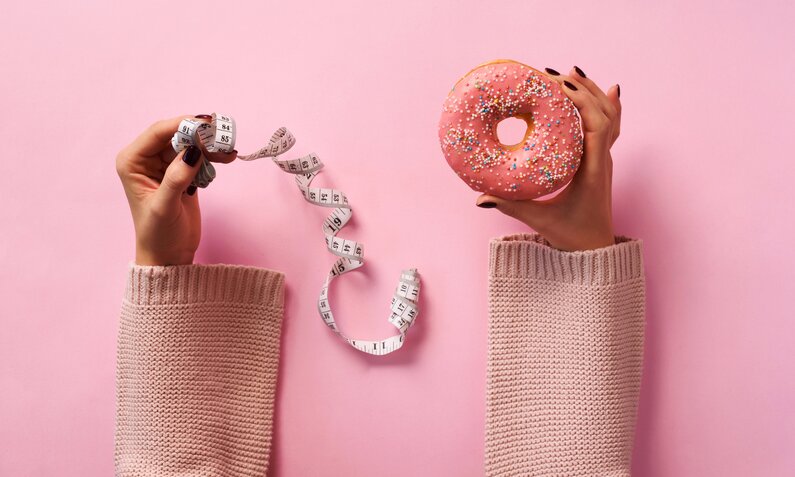 Hände halten Donut und Maßband | © gettyimages / jchizhe