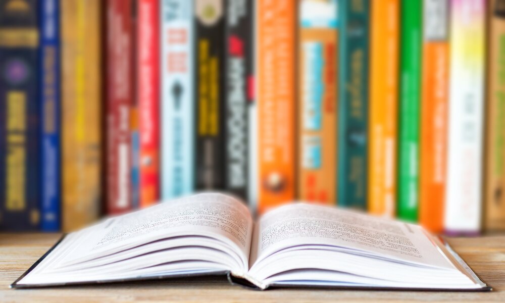 Buchreihe in einem Regal, davor ein offenes Buch | © Getty Images / Евгения Матвеец