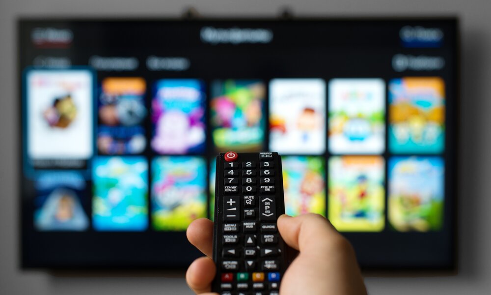 Smart TV im Hintergrund, Fernbedienung im Vordergrund, die auf den Fernseher zeigt | © Getty Images / M-Production