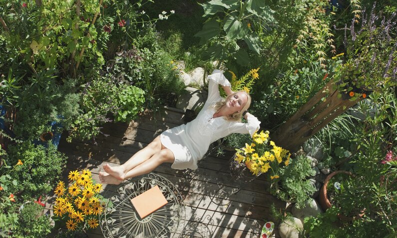 Frau liegt entspannt im Garten, um sie herum sind verschiedene Wildblumen und Pflanzen  | ©  Getty Images / Hans Huber