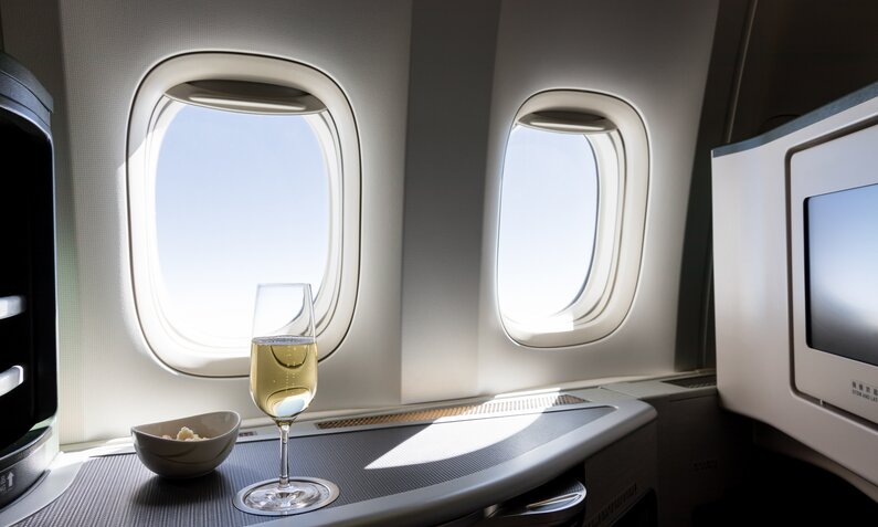 Flugzeugfenster in der Business Class, davor ein Glas Champagner und eine Schale mit Snacks | ©  Getty Images / jeremietardieu / 500px