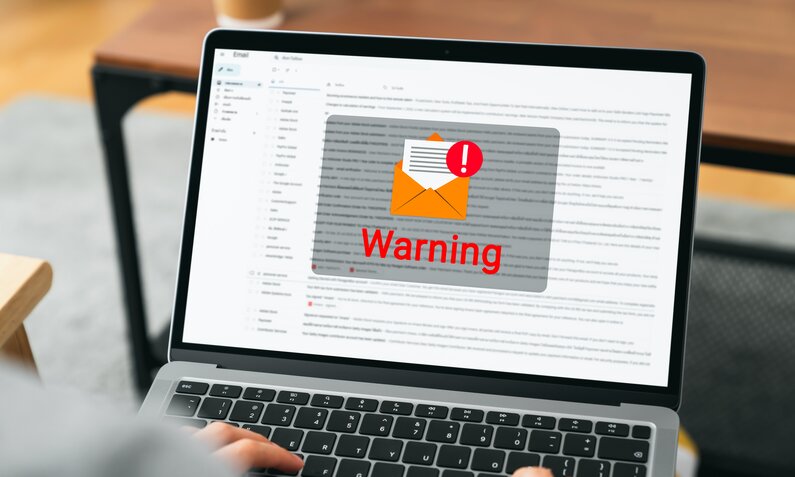 Der Bildschirm eines Laptops zeigt eine Warnung vor dem Hintergrund eines Email-Symbols. | © Getty Images/patcharin innara