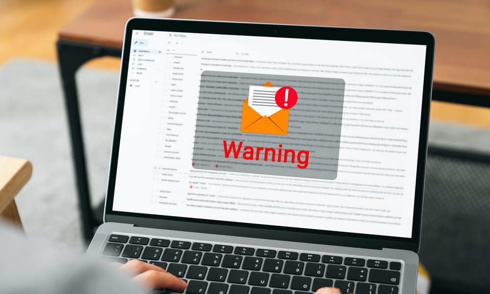 Der Bildschirm eines Laptops zeigt eine Warnung vor dem Hintergrund eines Email-Symbols. | © Getty Images/patcharin innara