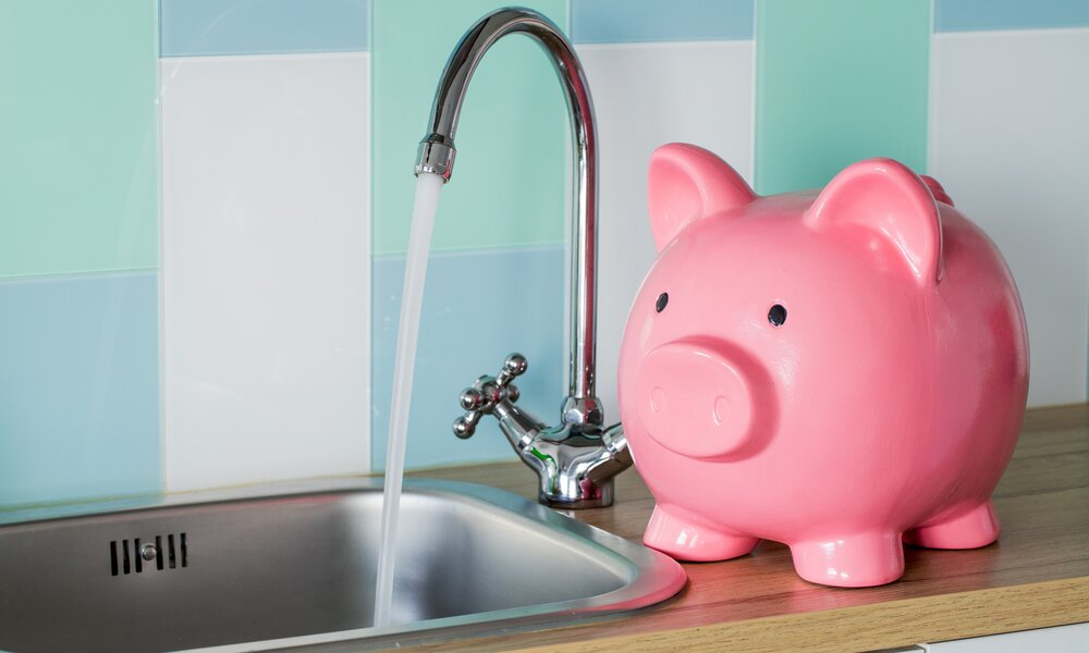 Sparschwein steht neben einem laufenden Wasserhahn  | ©  Getty Images / Andrzej Rostek