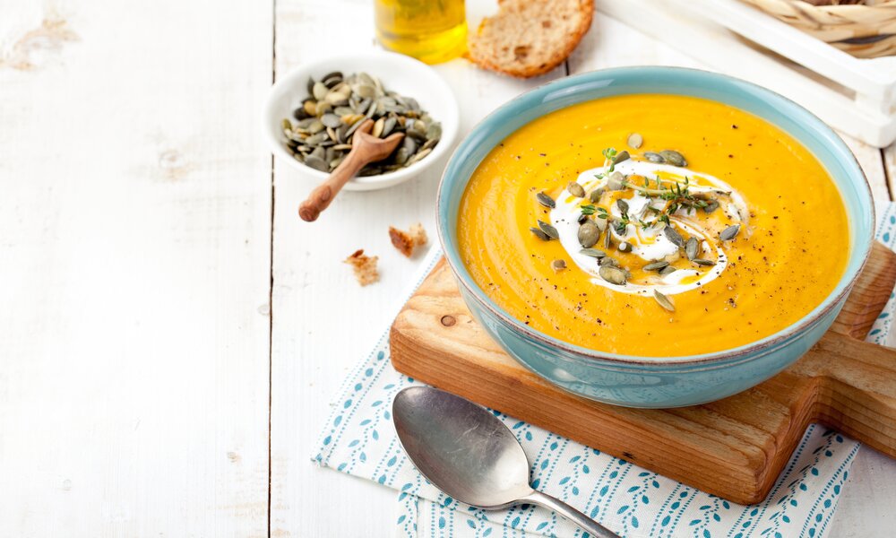 In einer blauen Schale befindet sich cremige Kürbissuppe, bestreut mit Kürbiskernen und Thymian. Ein Klecks Schmand ist ebenfalls auf der Suppe. | © Getty Images / AnnaPustynnikova