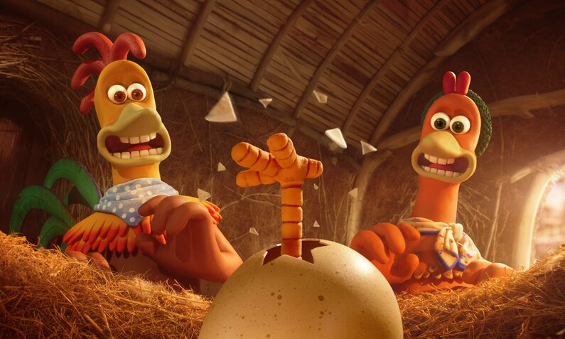 Zwei Animationshühner stehen im Stall im Stroh und schauen überrasscht auf ein Ei, aus dem ein Hühnerfuß ragt in einer Szene aus dem Netflix-Film "Chicken Run: Operation Nugget" | © Netflkx