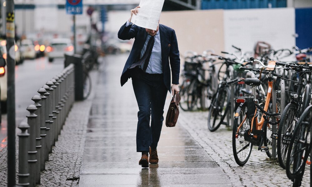Mann läuft in Anzug durch den Regen und hält sich eine Akte über den Kopf | ©  Getty Images / Willie B. Thomas