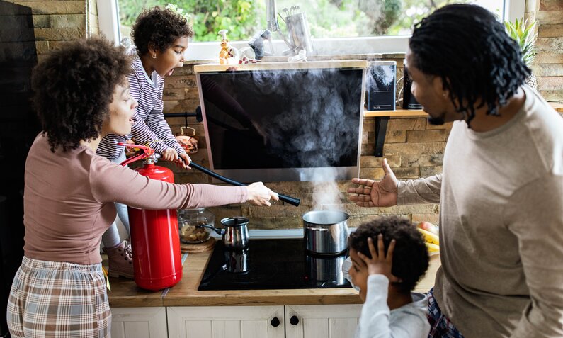 Familie löscht mit einem Feuerlöscher einen kleinen Küchenbrand | ©  Getty Images / skynesher