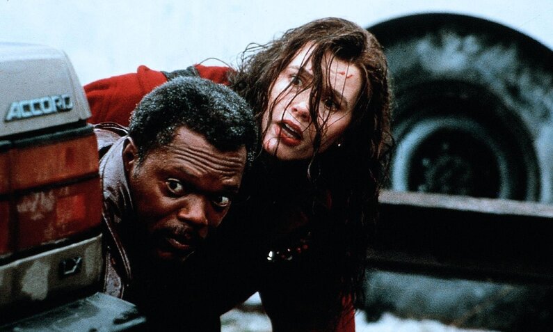 Samuel L. Jackson und Geena Davis sehen zerzaust und angespannt hinter einem Auto hervor in einer Szene aus dem Kinofilm "Tödliche Weihnachten" | © ddp images